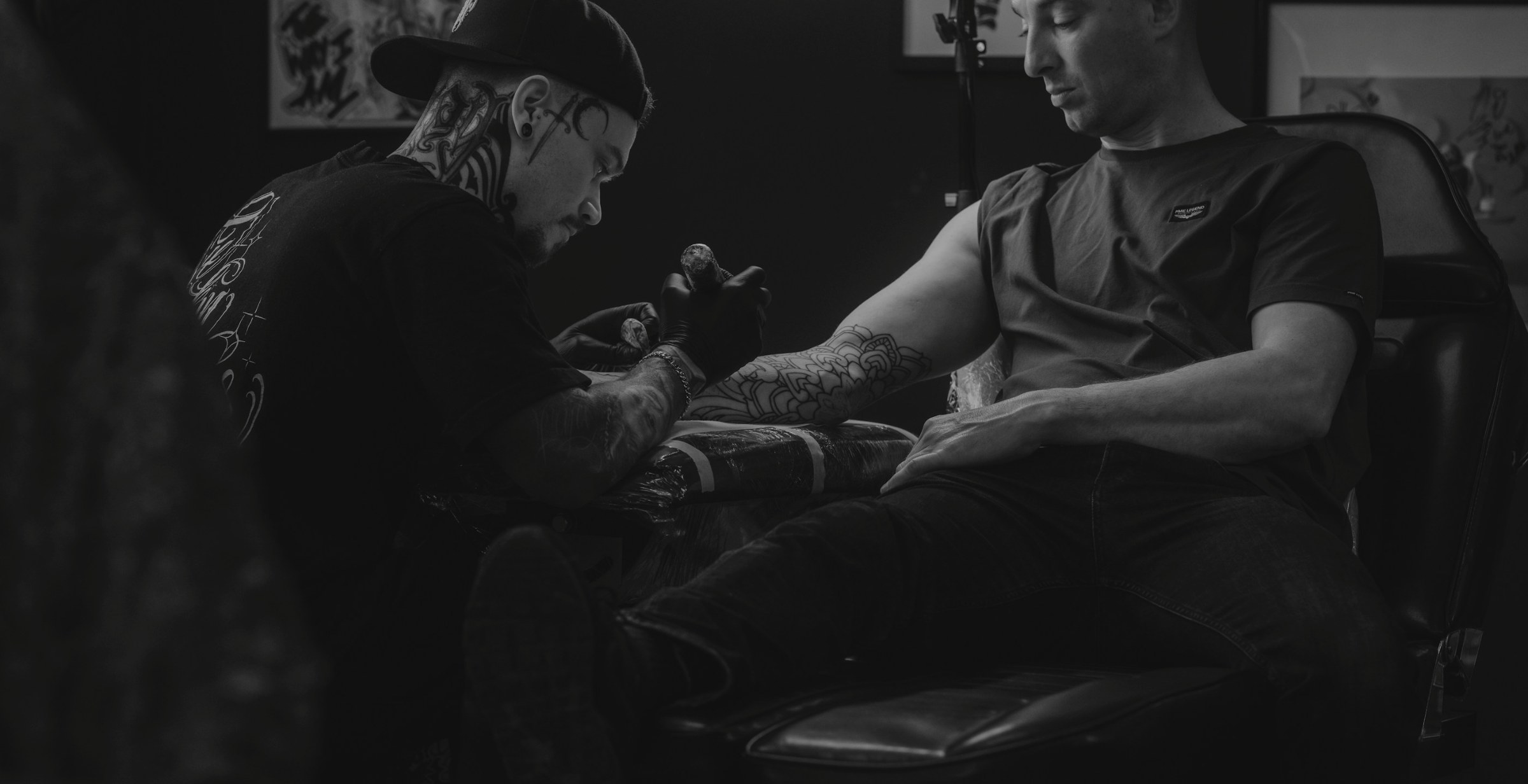 Tattoo artist working on a client's arm in a dark tattoo studio